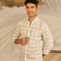 Man wearing a checkered shirt standing under a straw umbrella with a neutral background